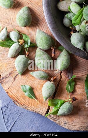 Fresh unripe almonds on the wooden background. Fresh raw green almonds in the metal bowl. Top view. Stock Photo