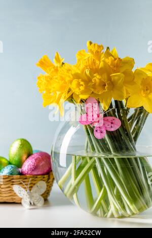 Easter themed yellow daffodils in round glass vase on table with light blue background. Selective focus. Copy space Stock Photo