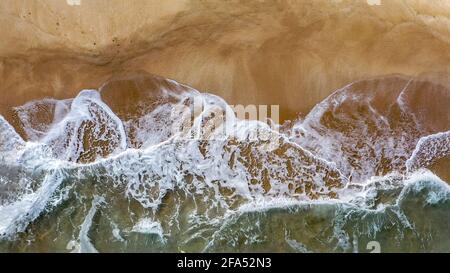 Aerial image of sea waves crashing on a beach in a summer afternoon