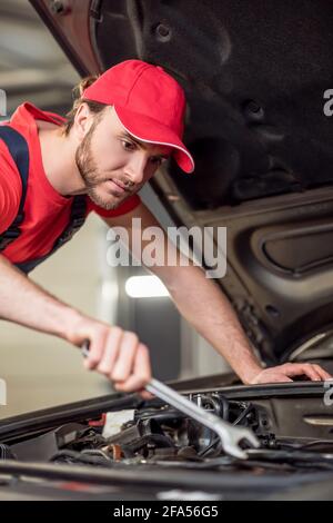 Man in overalls near hood repairing car Stock Photo