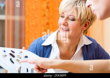 Older woman or female pensioner with a hearing problem make a hearing test and may need a hearing aid, she looking on a selection of them Stock Photo