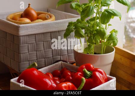 A fragment of a window in the kitchen. Vegetables baskets and bowls, next to basil in a pot. Stock Photo