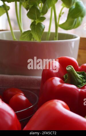 A fragment of a window in the kitchen. Vegetables baskets and bowls, next to basil in a pot. Stock Photo