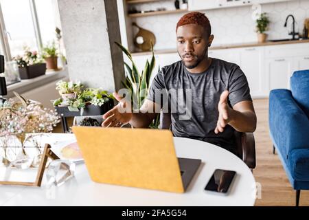 Serious male freelancer using laptop, having important video meeting with colleagues, working from home. Concentrated young businessman discussing a Stock Photo