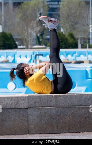 A very fit woman does crunch exercises on a ledge near the Unisphere in Flushing Meadons Corona Park in Queens, New York City. Stock Photo