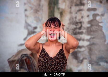 Portrait of Worried beautiful stressed young brunette woman suffering from a migraine, screaming loud out, hands on head looking up, people. Stock Photo