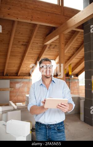 male architect middle age with black glasses stands on construction site in loft house and holds his tablet Stock Photo