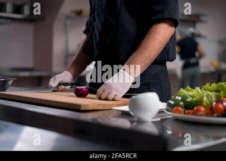 chef cook in medical gloves prepare greek salad or chop vegetables at kitchen  Stock Photo