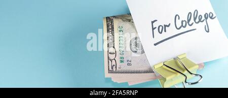 banner with text written note FOR COLLEGE with dollars cash money in clip, on copy space blue background - concept of financial planning to save money Stock Photo