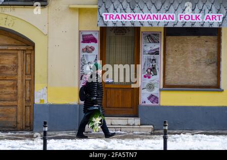 BRASOV, ROMANIA - 07 April 2021 - A woman walks past a closed-down Transilvanian Folk Art shop in the Historic Centre of Brasov, Romania. Many busines Stock Photo