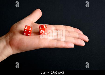 Red dices on the male palm on black background, close up. Board games. Stock Photo