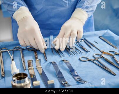 Close up of plastic surgeon in sterile gloves getting ready medical instruments for operation. Doctor preparing scissors, forceps and scalpels for surgery. Concept of plastic surgery preparation.