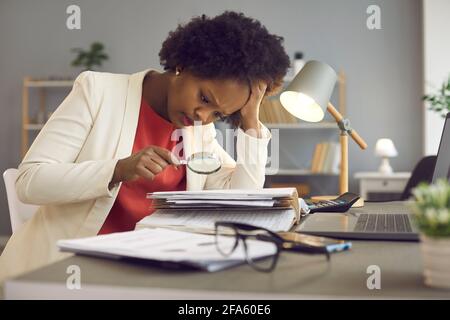 Focused woman uses a magnifying glass to check documents and look for an error in the accounts. Stock Photo
