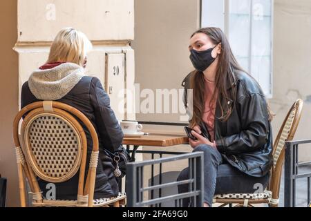 Two girls with masks sitting and drinking coffee at an outdoor bar, café or restaurant after quarantine restrictions Stock Photo