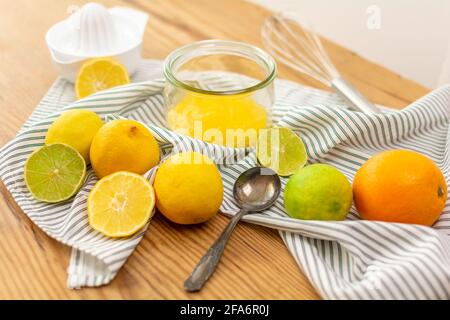 A lot of citrus fruits like lemons, oranges and limes on a wooden table ready to be squeezed for juice or for baking, a glass wtih lemon curd. Stock Photo