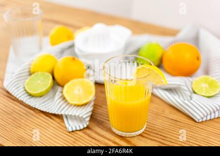 A glass of fresh orange juice on a wooden table with citrus fruits like lemons, oranges, limes and a kitchen towel. Stock Photo