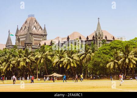 Mumbai, Maharashtra, India : A group of young men plays cricket at the Oval Maidan park in Churchgate district. High Court in background. The building Stock Photo