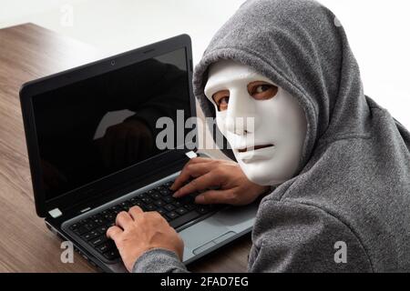 Thief hacker in mask stealing personal information from laptop. Concept hacking. Stock Photo