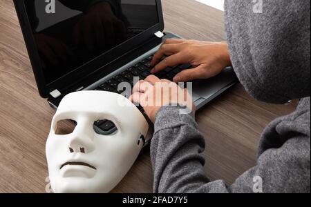 Thief hacker in mask stealing personal information from laptop. Concept hacking. Stock Photo