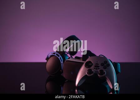 Set of joystick, VR helmet and headphones on dark violet background Stock Photo