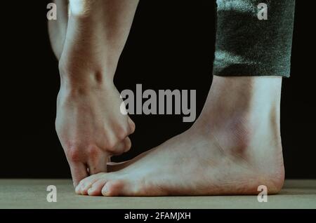 Close up of feet and fingers bound to big toes yoga pose padangusthasana on a black background Stock Photo