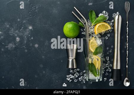 Mojito or Lemonade cocktail in highball glass with ice cubes, mint and lime on black stone background with shaker and beaker. Menu bar. Space for text Stock Photo