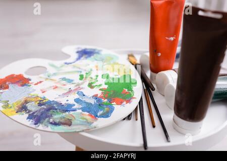 paintbrushes and palette near tubes with paint on coffee table Stock Photo