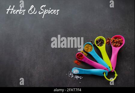 Multicolored measuring spoons with spices: chili flakes, a mix of pepper peas, curry, paprika and coarse sea salt. Black chalk board background with i Stock Photo