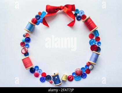 Wreath is made of buttons and threads of red and blue colors with pins and a bright bow of satin ribbon at the top. Copy space. Stock Photo