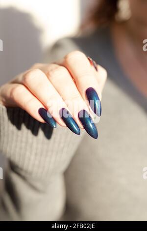 Female hand with long nails and light dark turquoise manicure with bottles of nail polish Stock Photo