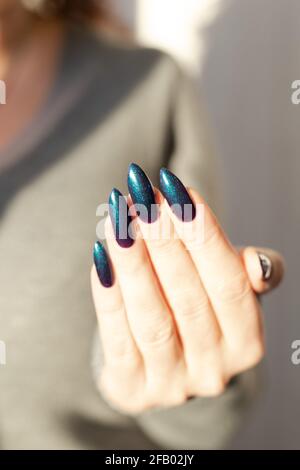 Female hand with long nails and light dark turquoise manicure with bottles of nail polish Stock Photo