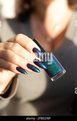 Female hand with long nails and light dark turquoise manicure with bottles of nail polish Stock Photo