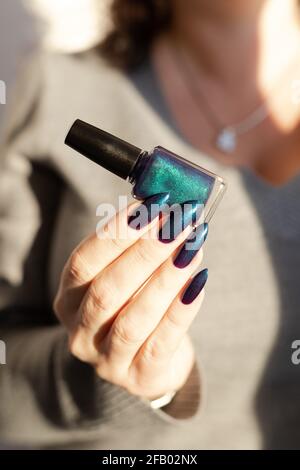 Female hand with long nails and light dark turquoise manicure with bottles of nail polish Stock Photo