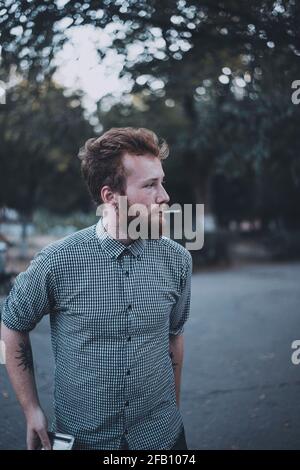 Curly young bearded man with tattoo smoking a hand rolling tobacco  Stock Photo