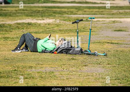 WIMBLEDON LONDON, UK. 23 April, 2021. A woman lying on the grass on a beautiful sunny day on Wimbledon Common, London as forecasters predict warmer weather with temperatures expected to reach 19celsius over the weekend in London and the South East of England. Credit: amer ghazzal/Alamy Live News Stock Photo