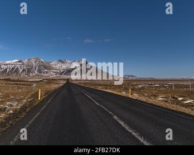 Beautiful view of straight, empty road (route 54) with diminishing perspective on Snaefellsnes peninsula, western Iceland with rough, snowy mountains. Stock Photo