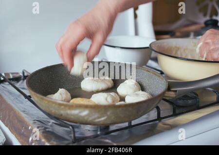 Hand puts a doughnut in oil in frying pan on gas stove Stock Photo