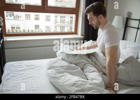 young man reading a newspaper with news in bed Stock Photo