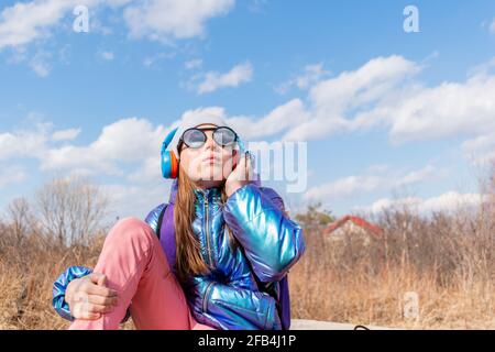 Teenage girl in mirrored sunglasses looks into the sky. Wellness concept. Child listens to music and sings Stock Photo