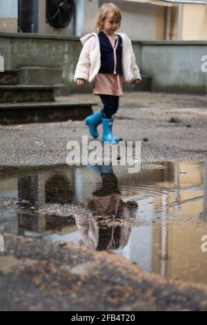 Reflection of a girl in rubber boots walking next to puddle Stock Photo