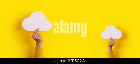 Two hands holding paper cloud over yellow background, panoramic image, cloud storage concept Stock Photo