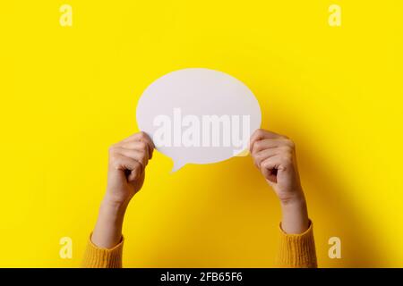 Dialogue icon, blank speech bubble in hand over yellow bacckground, layout image Stock Photo
