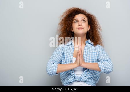 curly woman with praying hands looking up on grey background Stock Photo