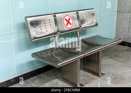 Picture of empty waiting chairs with social distancing sign, red cross mark. Metallic chair with social distancing symbol on seat in a metro station d