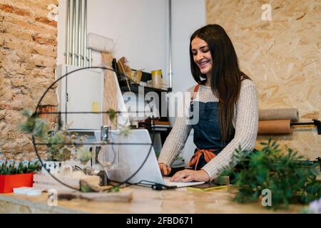 Cheerful female owner smiling while using laptop in flower shop Stock Photo