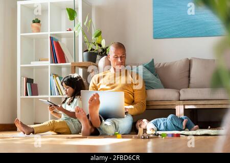 Father working on laptop while sitting by daughters at home Stock Photo