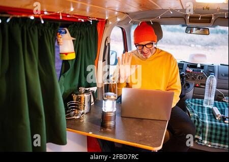 Smiling mature man waving hand during video call through laptop in motor home Stock Photo