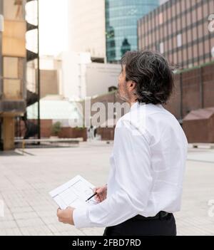 Male architect with blueprint looking up in office park Stock Photo