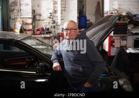 Confident male mechanic with hand in pocket leaning on car at workshop Stock Photo