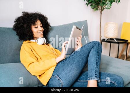 Relaxed young woman using digital tablet while sitting on sofa at home Stock Photo